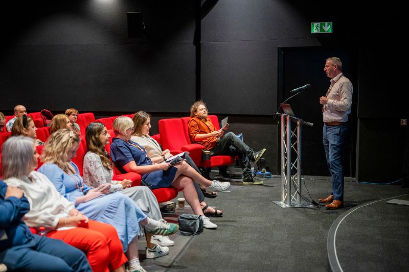 Rory Bonnar speaking at a podium to event attendees in the QFT screen 1 at Behind the Scenes at Queen's
